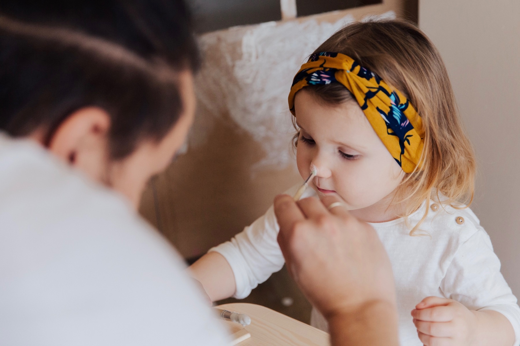 A young girl and her father play together with face paints.