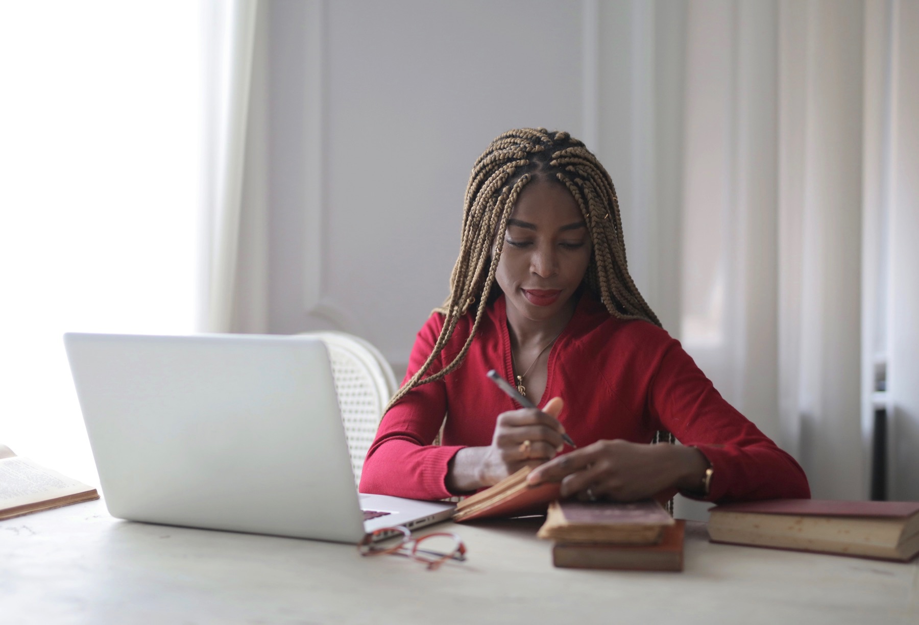 Woman takes notes at her desk in front of a laptop.