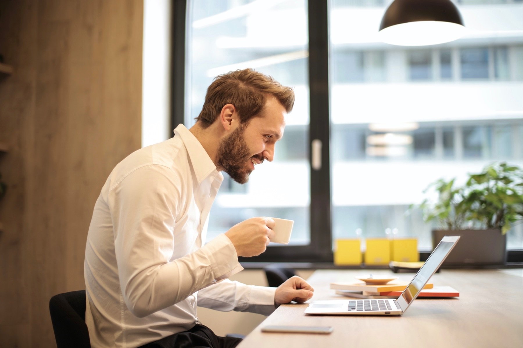 A man drinks a tea while at his computer.