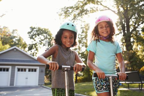 Two young girls playing on scooters in a driveway