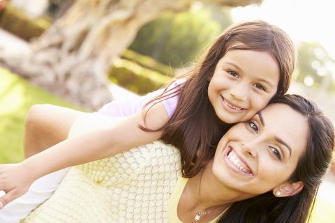 Smiling mother giving happy daughter a piggy back ride outside during the spring