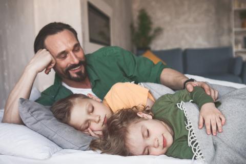 Father smiles at his children as they sleep beside him.