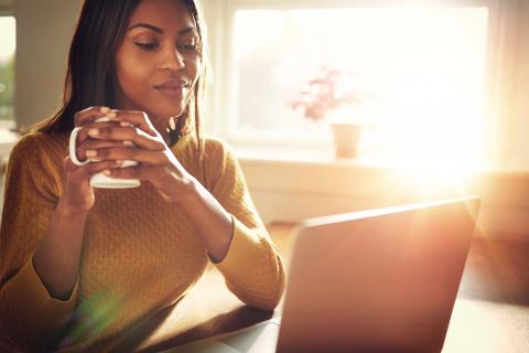 A woman sips coffee while working at her computer.