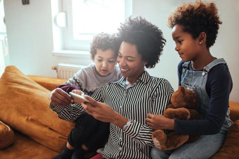 Mom and kids look at pictures on a phone while hanging out on the couch.