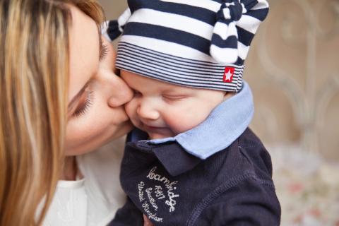 A mother kisses her infant child on the cheek.