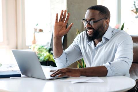 Man in light blue shirt waving to someone on a virtual meeting