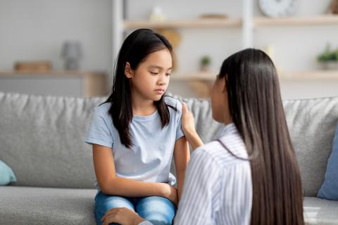 A young girl looks sadly towards the ground as her mother attempts to comfort her.