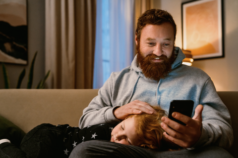 Dad holding phone with son on couch.