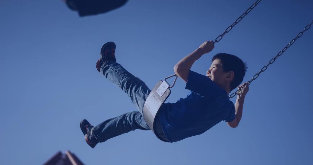 Young boy laughs as he swings outside on a clear spring day.