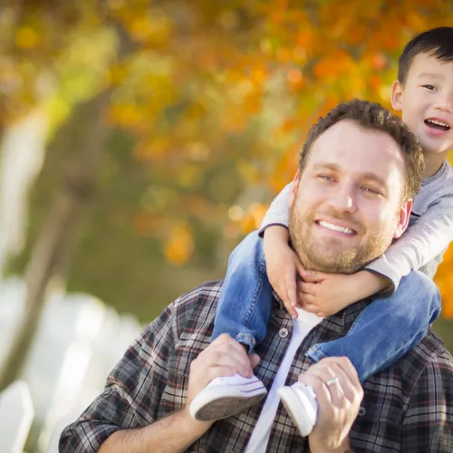Father gives young son a piggy back outside during the fall.