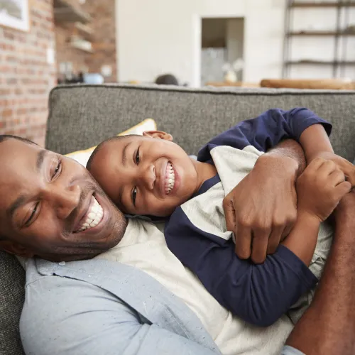 Father holds son on couch while both laugh