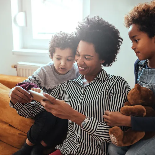 Mom and kids look at pictures on a phone while hanging out on the couch.