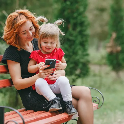 Mom holds daughter on park bench as they look at a phone together