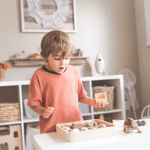 A young boy cleans his play area by putting his toys into a small box.
