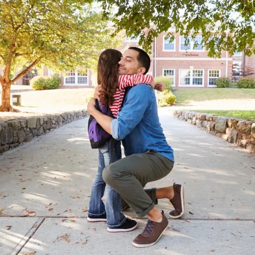 Dad hugging daughter on sidewalk. 