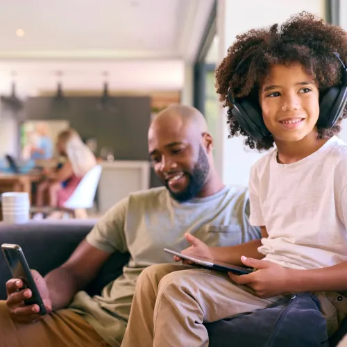 Young boy wearing headphones while sitting with his dad on the couch. 