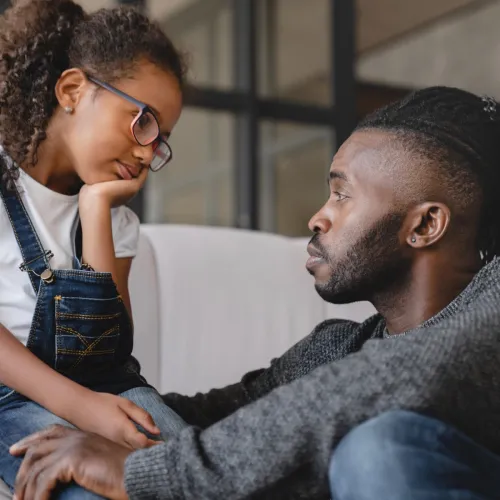 Dad listening to daughter as she sits on the couch. 