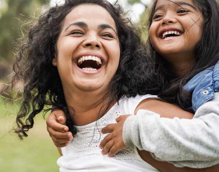 A mother smiles as she gives her young daughter a piggy back ride.