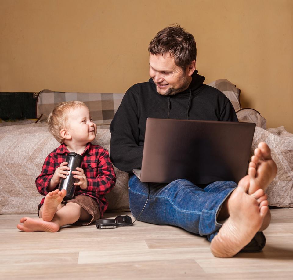 Father works on laptop as young son happily sits next to him.