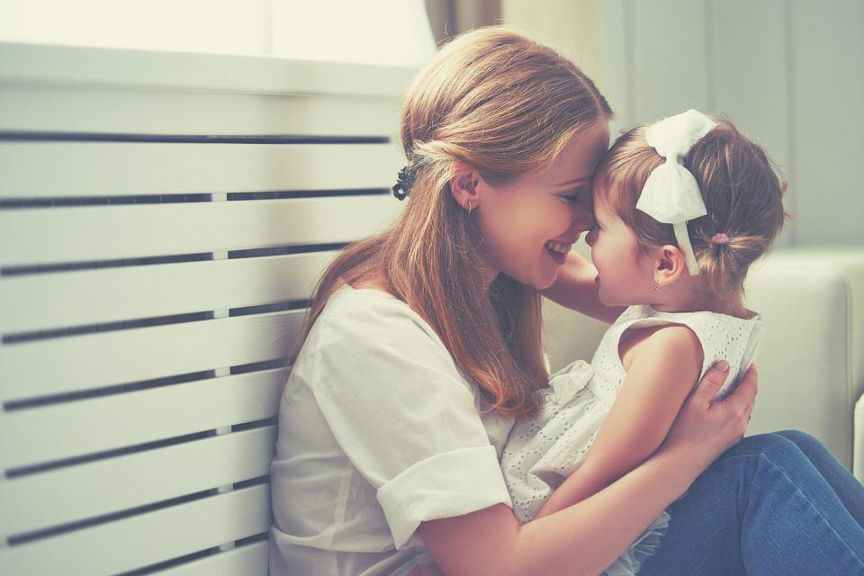 Young mother looks into daughter's eyes while holding her on her lap.