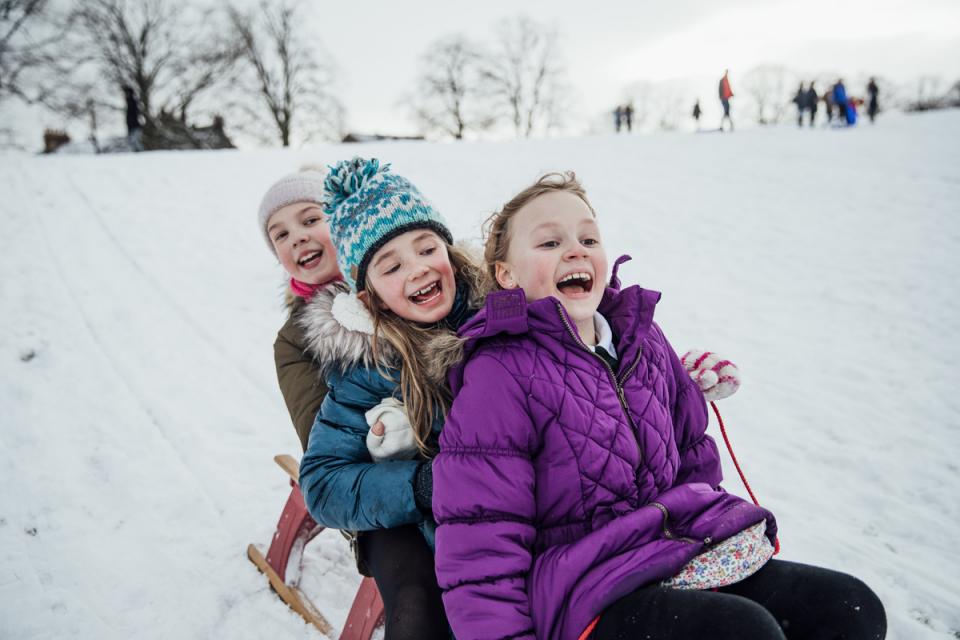 Three laughing girls sledding down a snow-covered hill.