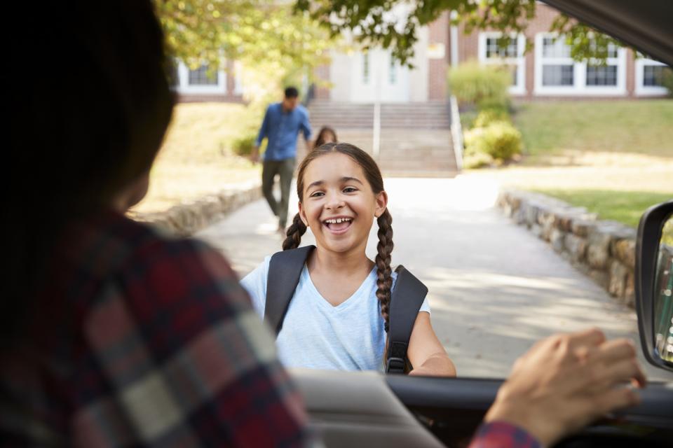 Young girl runs up to parent's car with a smile on her face outside of her school.