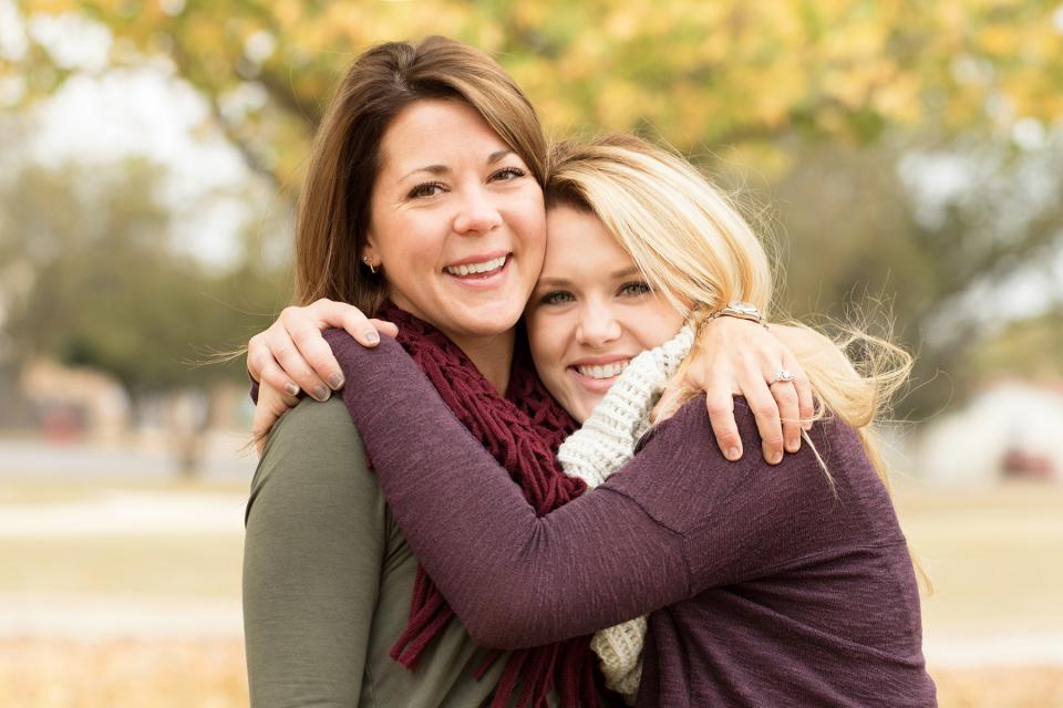 Mother and adult daughter embrace outside on a fall day