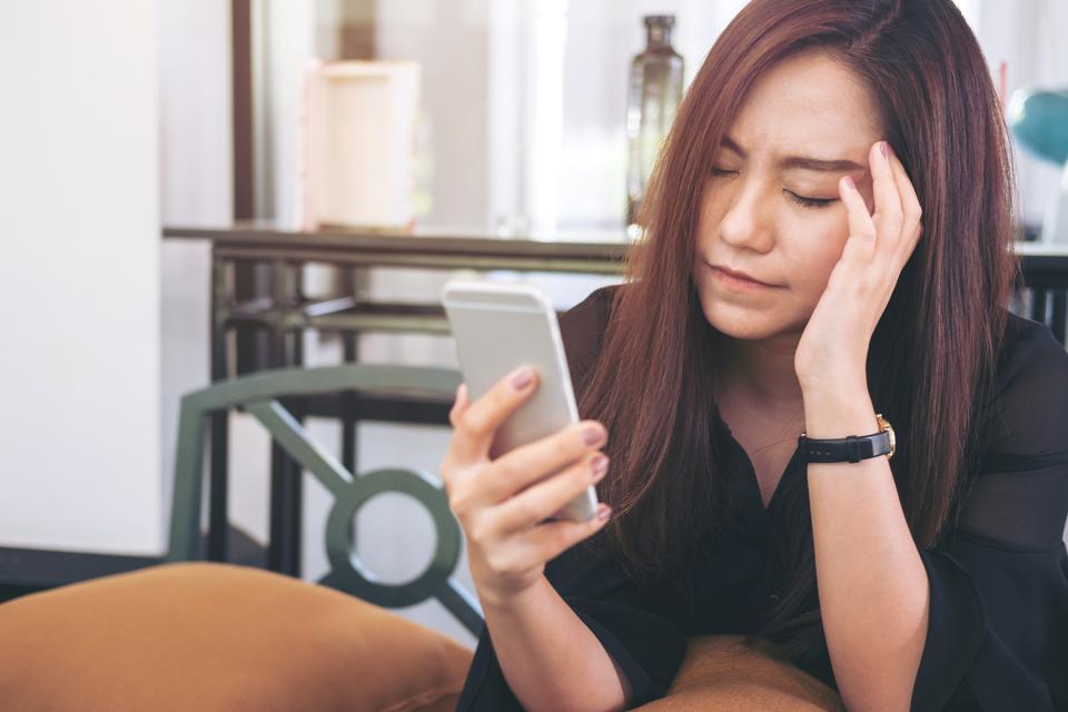 Stressed woman rubs her temple as she looks at her cell phone