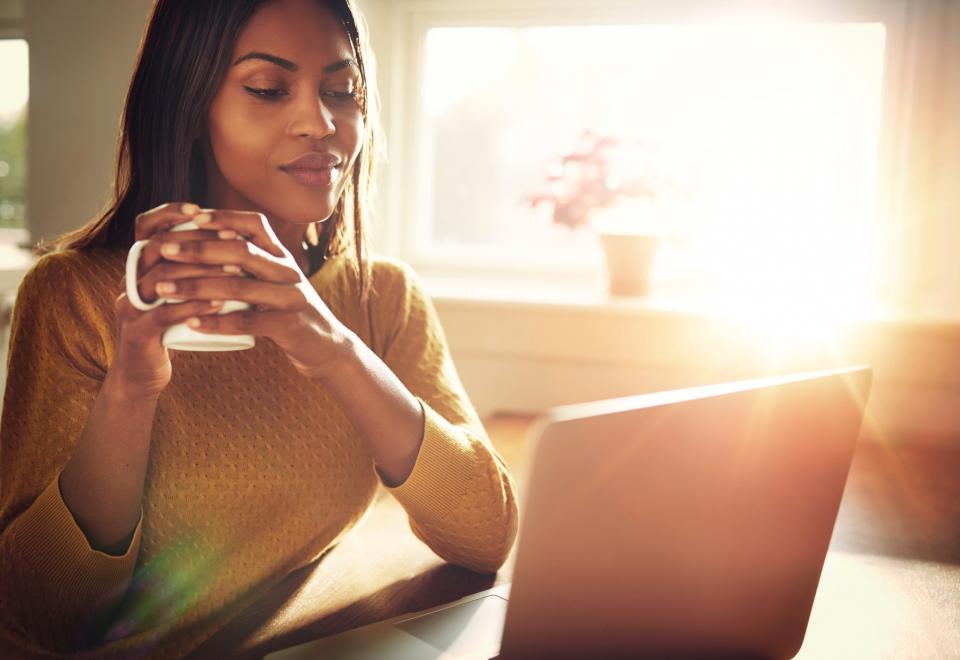 A woman sips coffee while working at her computer.