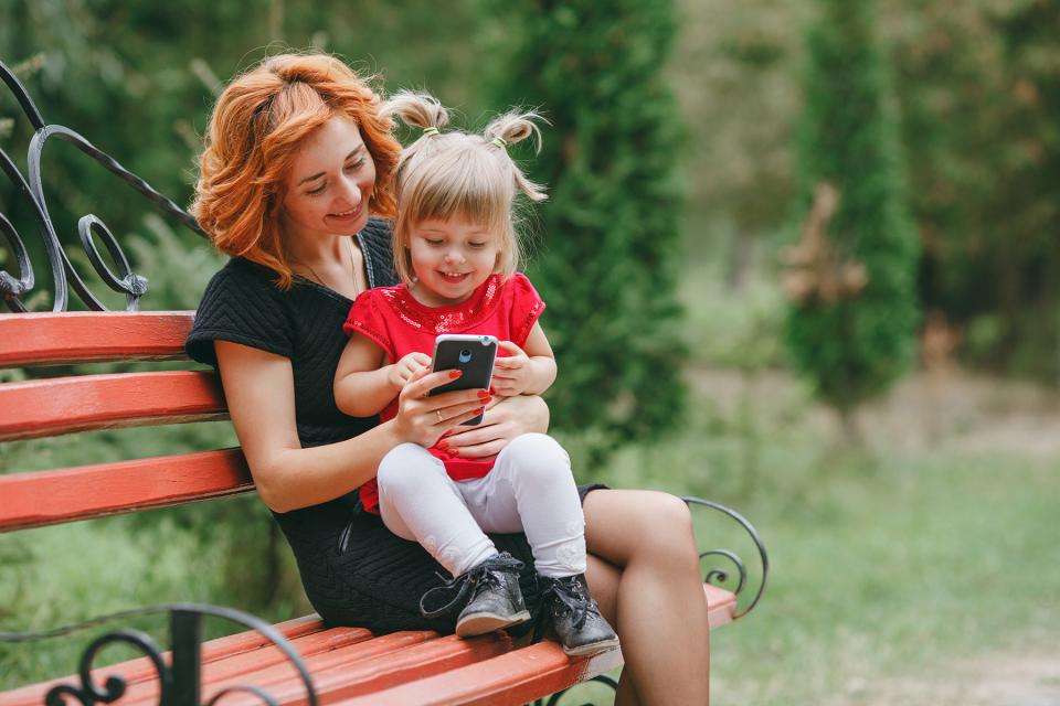 Mom holds daughter on park bench as they look at a phone together