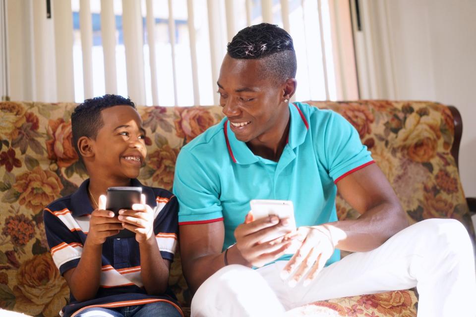 Uncle and nephew use their phones together on the couch.