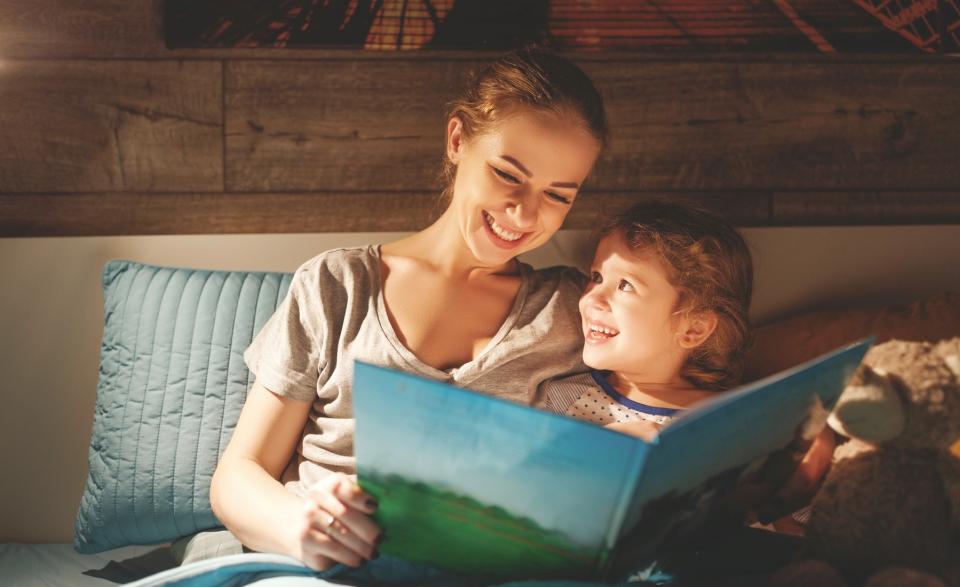 A woman reads a book to her child in bed.