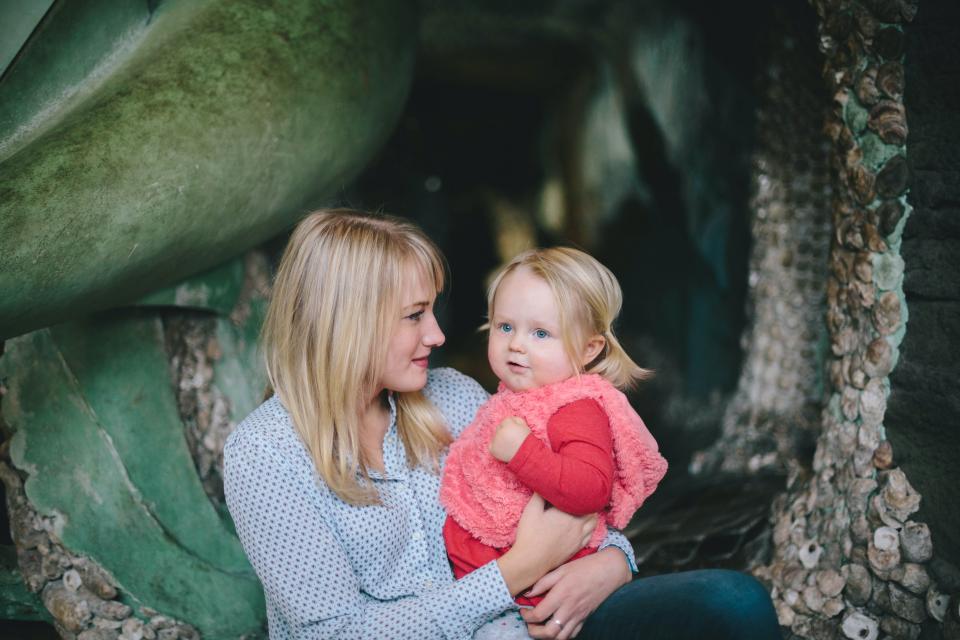 woman and young daughter in pink vest outside by a large green plant