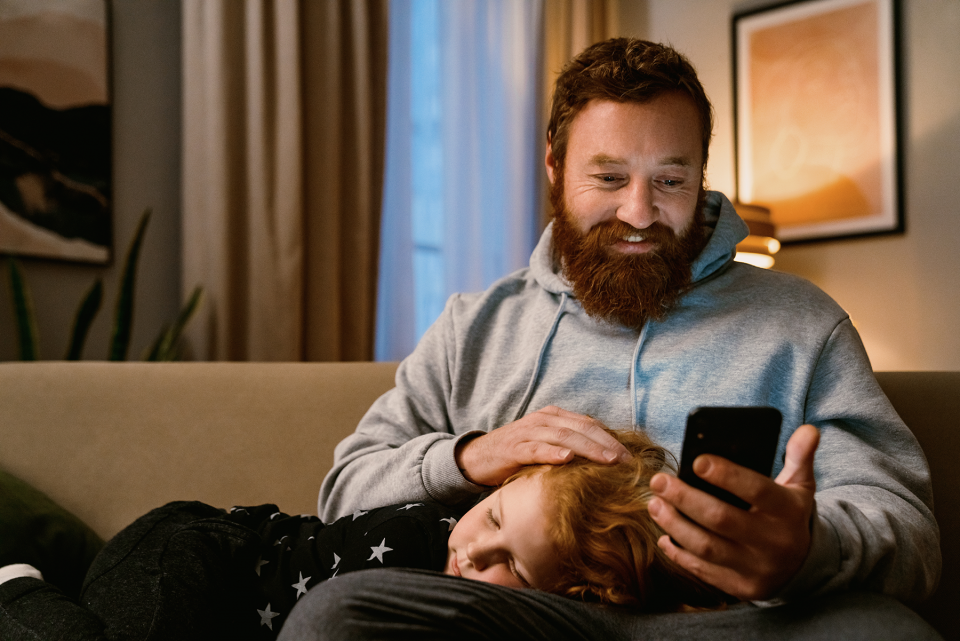 Dad holding phone with son on couch.