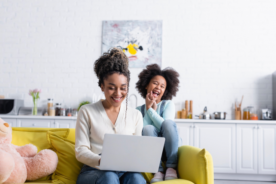 Mom on laptop with daughter on couch.
