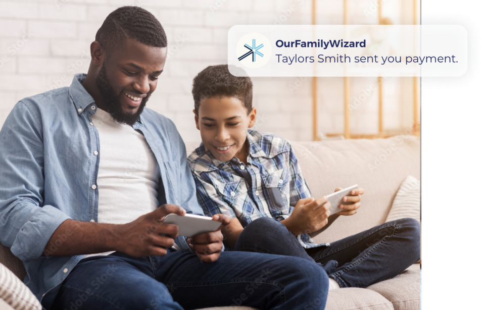A father and child look at the father's smartphone alongside an example of an OurFamilyWizard app notification about a new payment sent.